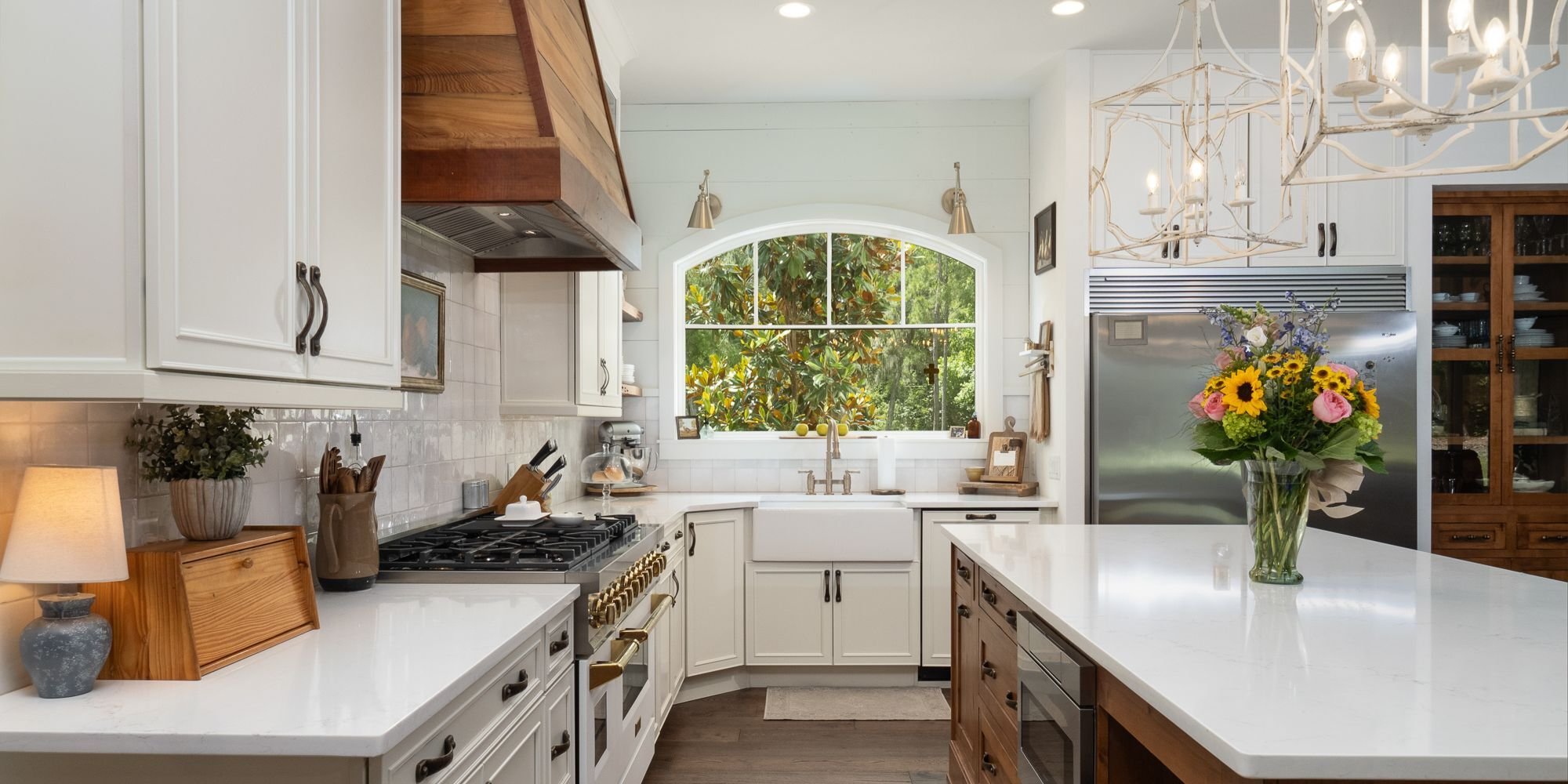 Custom kitchen remodel featuring a large island, a hood vent with a natural wood look, and a large window over the sink by Robinson Renovation & Custom Homes in Alachua County