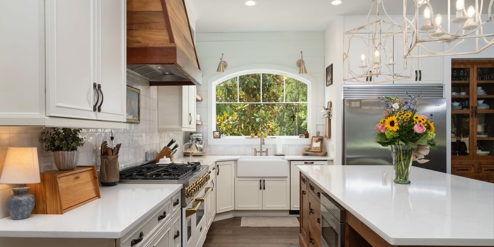 Custom kitchen remodel featuring a large island, a hood vent with a natural wood look, and a large window over the sink by Robinson Renovation & Custom Homes in Alachua County