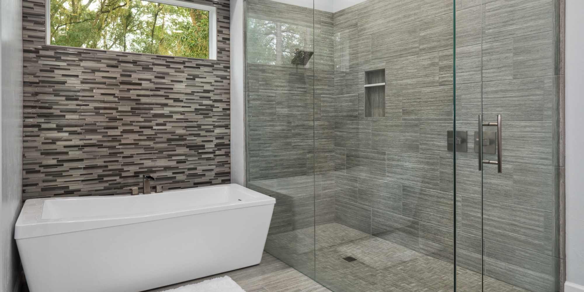 A renovated bathroom in a whole home remodel with a glass shower, white soaking tub, and a multicolored tile wall in Gainesville, FL by Robinson Renovation & Custom Homes