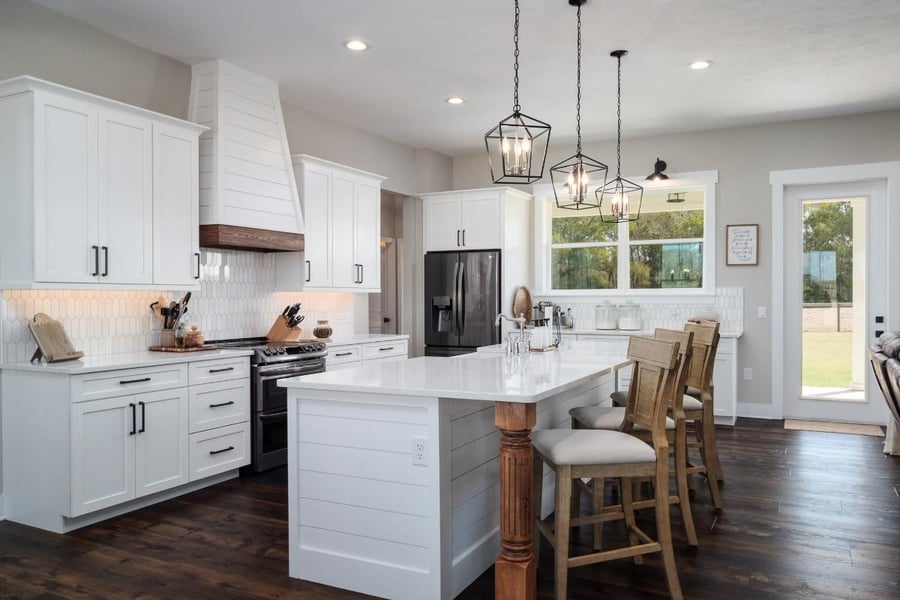 Traditional kitchen layout with a large hood, kitchen island with seating, pendant lights, and dark wood floors. 