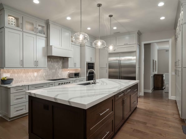 Gainesville kitchen renovation featuring white cabinetry, a large quartz island, stainless steel appliances, pendant lighting, and hardwood floors.